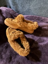 Women  s tan faux fur-lined moccasin slippers made of suede-like material.