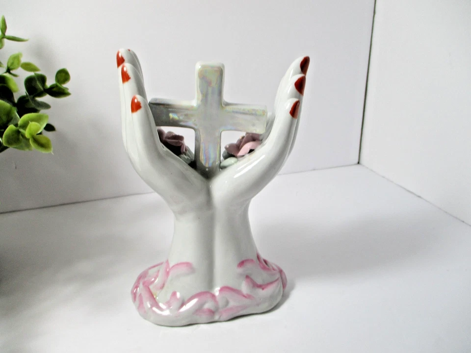 Dos manos de cerámica con clavos rojos sosteniendo una cruz y flores. Foto 2 de 4