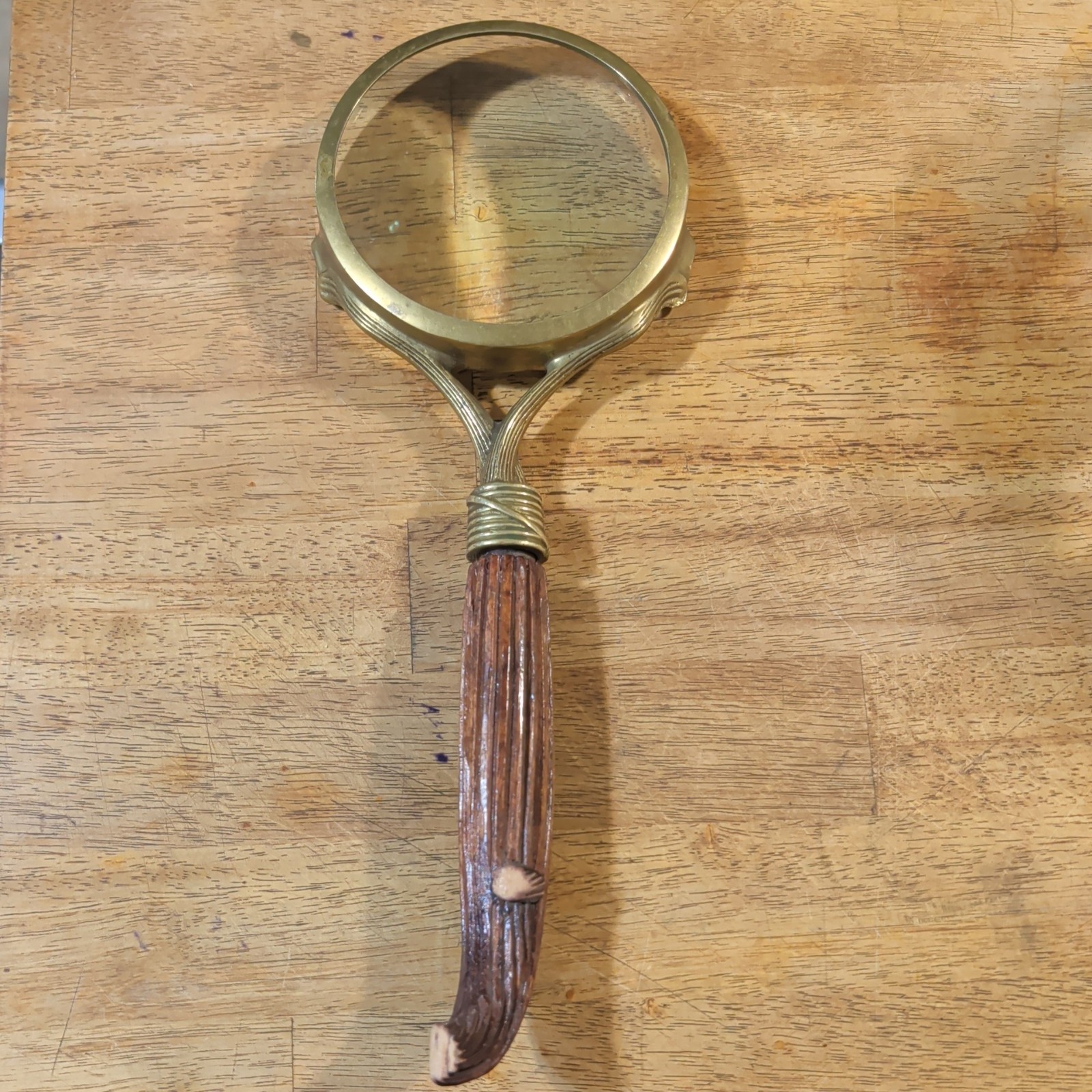 Antique brass magnifying glass with a carved wooden handle.