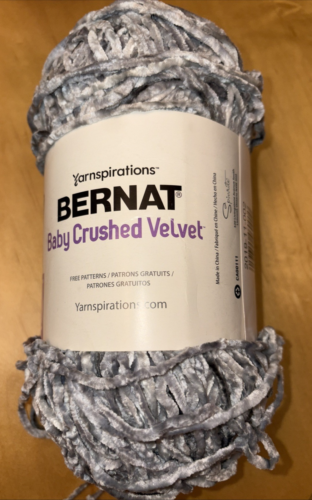 Grey mist Bernat Baby Crushed Velvet yarn ball with textured loops, wrapped in label showing brand name and floral accents.