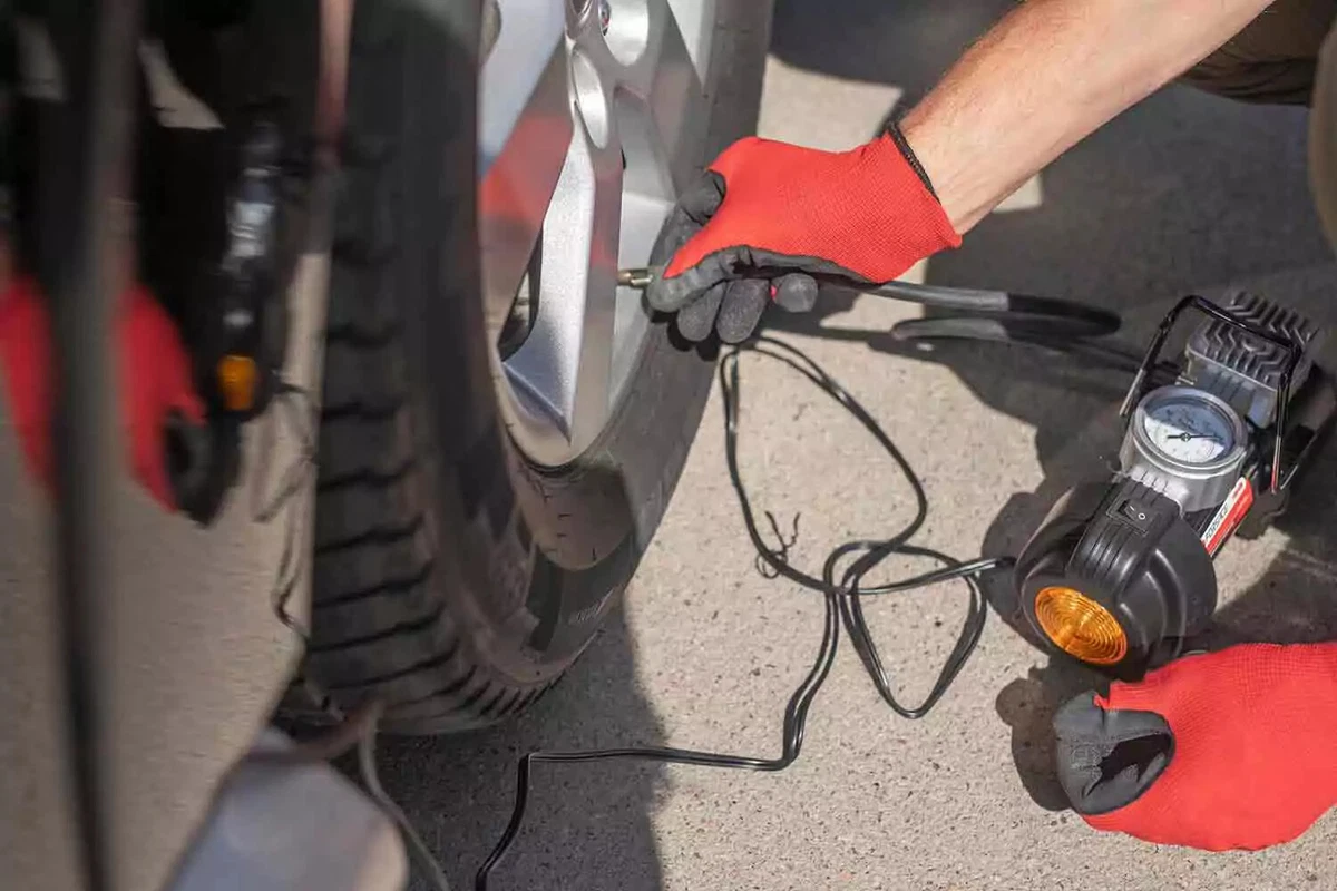 A driver wearing red and black protective gloves inflates a tire with a portable compressor.