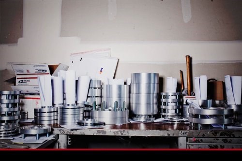Assorted silver Porsche 997 wheel spacers in clear boxes on a workbench, some with white labels reading “Adaptec Speedware Made in U.S.A.”