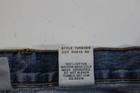 White fabric tag on blue jeans with yellow stitching, showing style 72RB30, cut R5814, and care instructions.