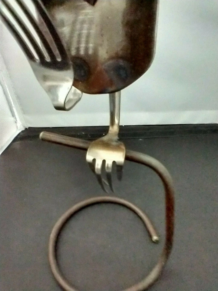 Búho esculpido sentado en soporte hecho de cucharas, tenedores, arandelas y metal Foto 3 de 4