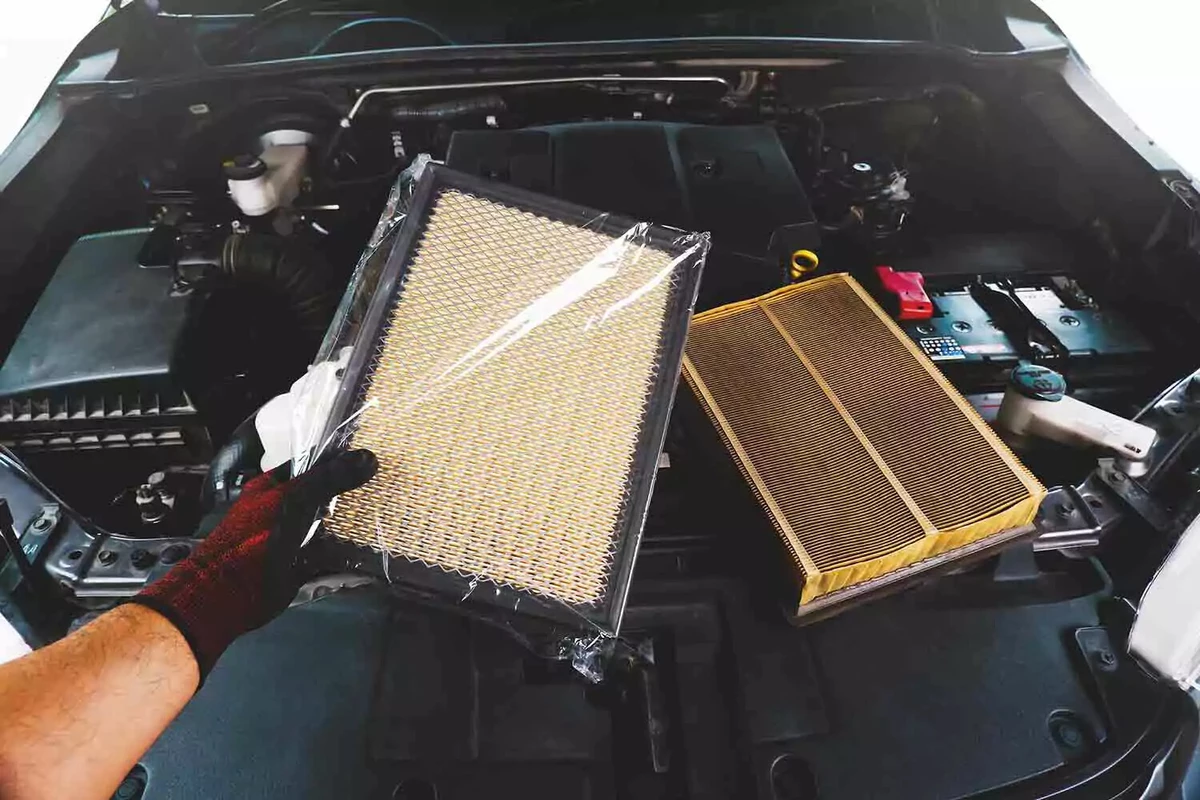 A mechanic holds a new plastic-wrapped air filter next to an old air filter that needs to be replaced.