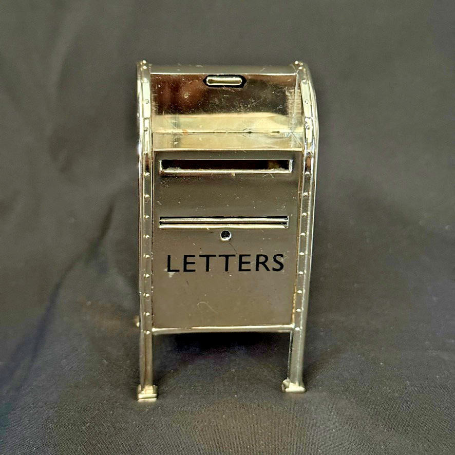 A Neiman Marcus-branded silver miniature mailbox that dispenses stamps — tiny, quirky, and surprisingly charming as a desk object.