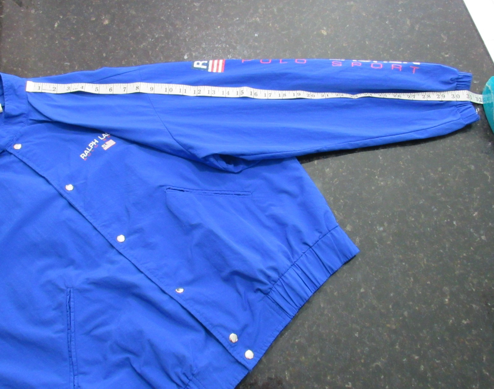 Blue Vtg 90s Polo Sport Ralph Lauren jacket with white “Polo Sport” text, sleeves, and elastic waistband.