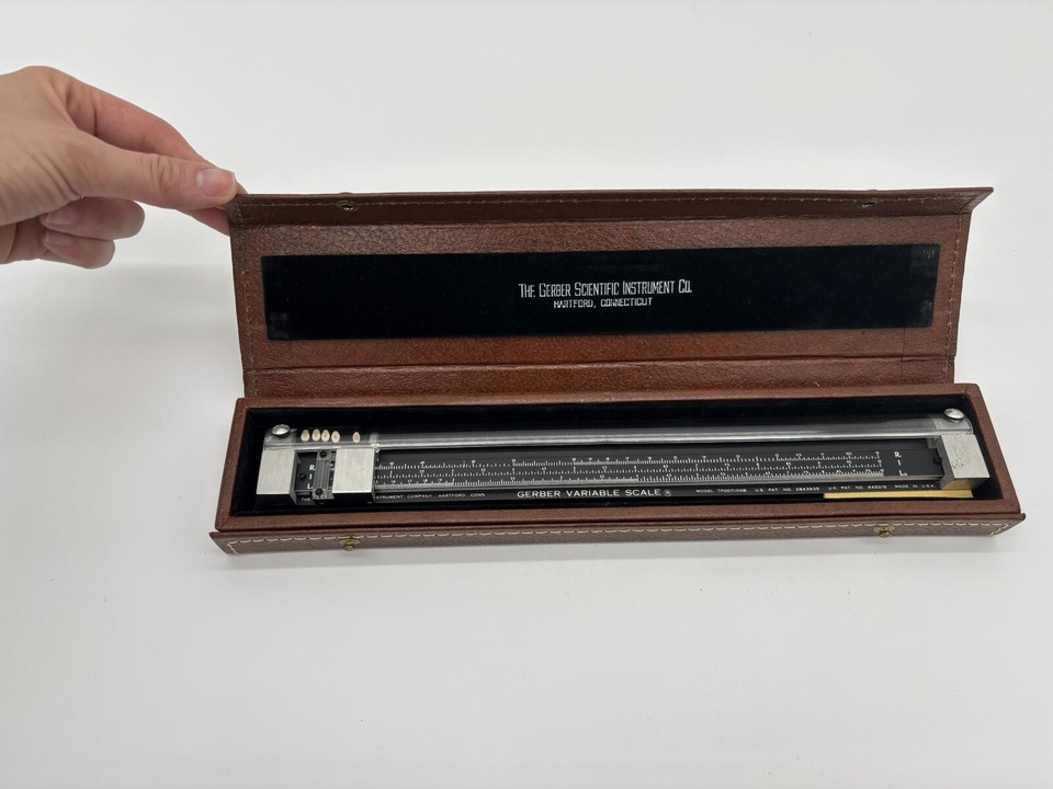A Gerber Scientific variable scale in its original leather case — a drafting-era precision tool that looks like a prop from a Cold War spy film.