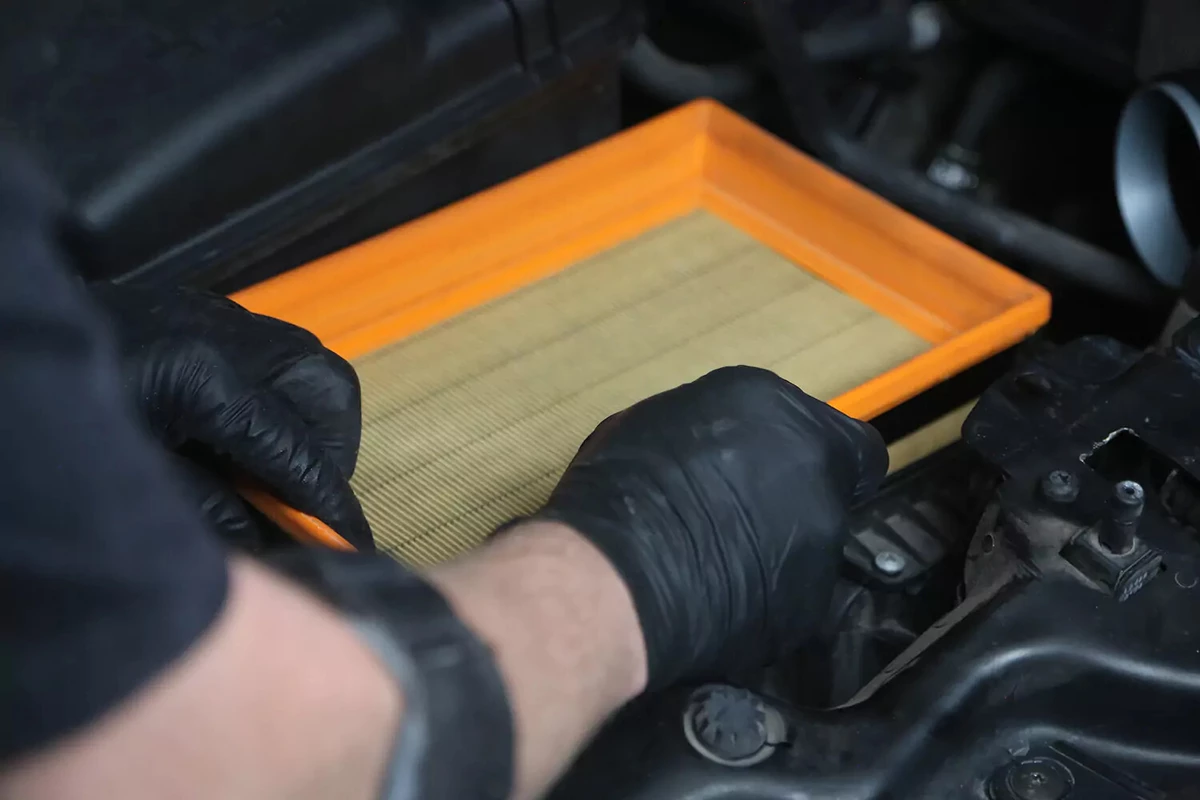 A mechanic wearing black gloves places a new air filter inside the filter box.