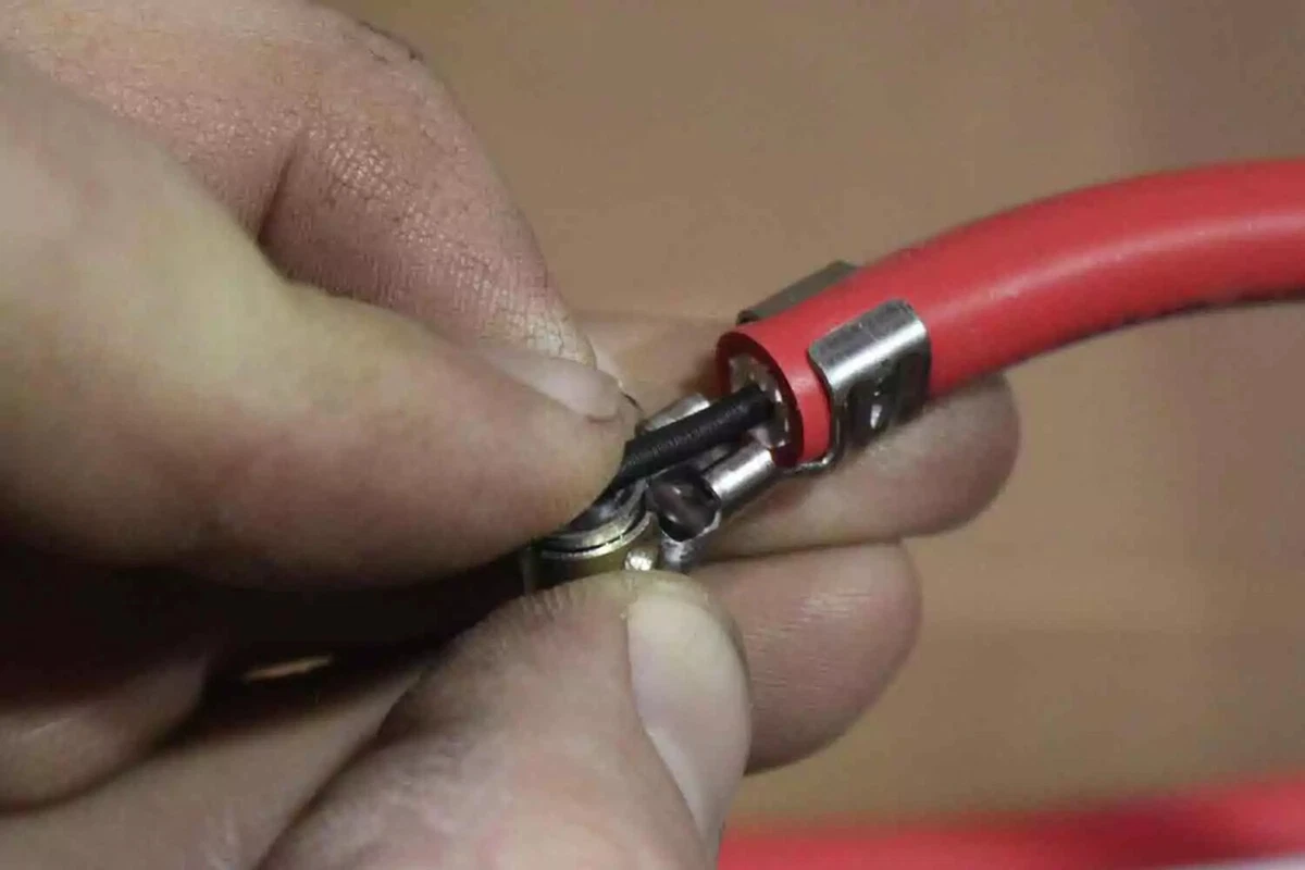 A close-up view of a mechanic holding a red ignition wire with an open end, exposing the inner support jacket and black suppression layer that covers the ignition wire’s core.