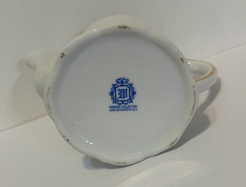 White porcelain teapot with ornate lid, gold rim, and blue floral medallion reading “Winrose Collection Hand Decorated in U.S.A.”