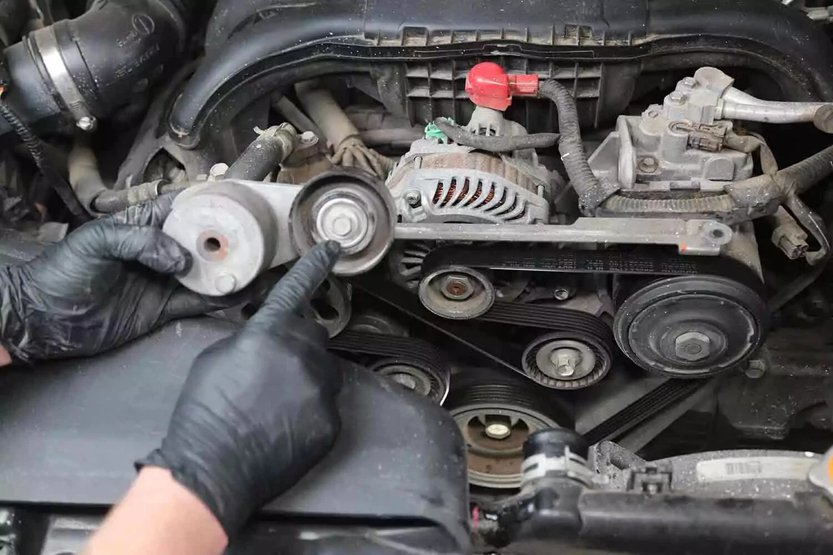 A mechanic wearing black nitrile gloves points to the tensioner’s bolt-on pulley.
