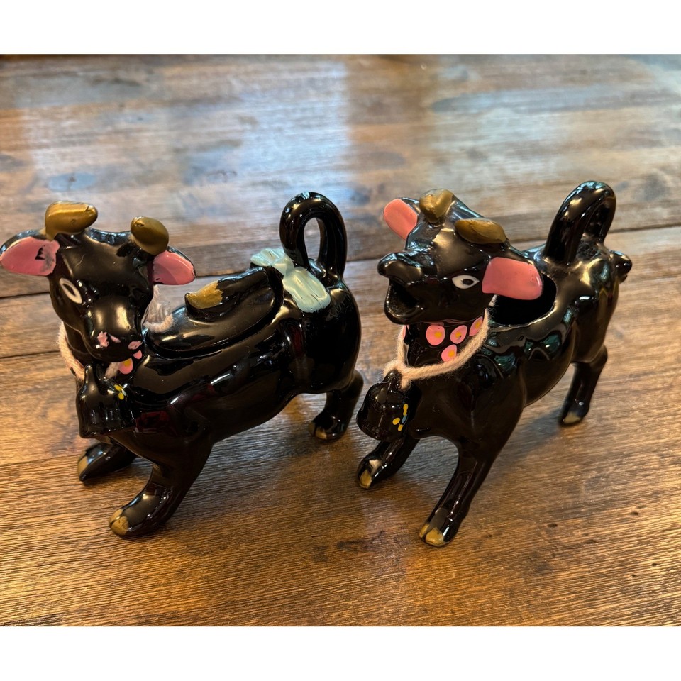 Glossy black ceramic cow creamer and sugar set with pink and gold accents — pure 1950s farmhouse kitsch that doubles as functional serveware.