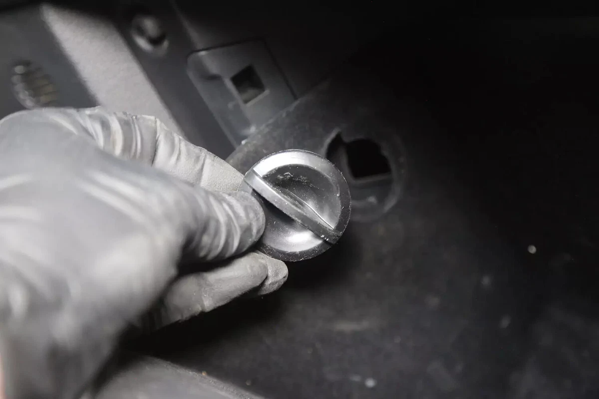 A mechanic wearing a black glove removes a stop from a vehicle's glove box.
