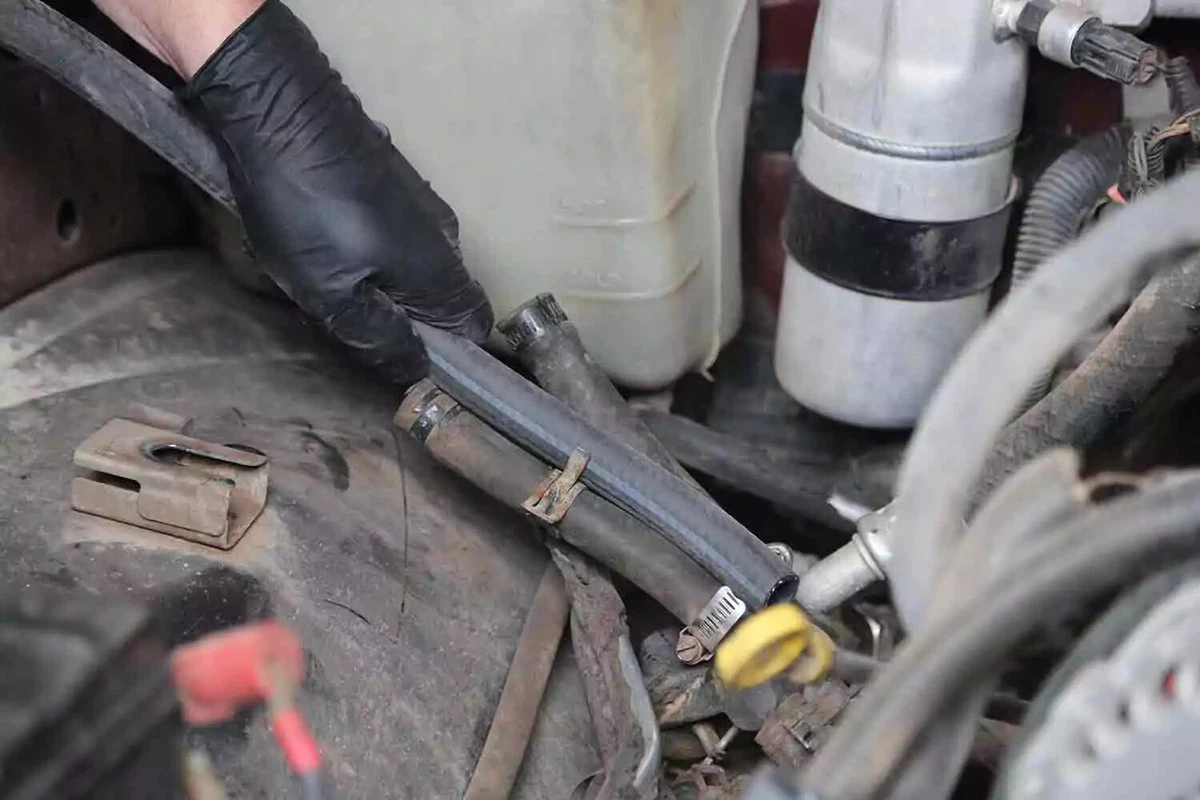 A mechanic wearing a black glove holds a length of new hose next to the old heater core hose.