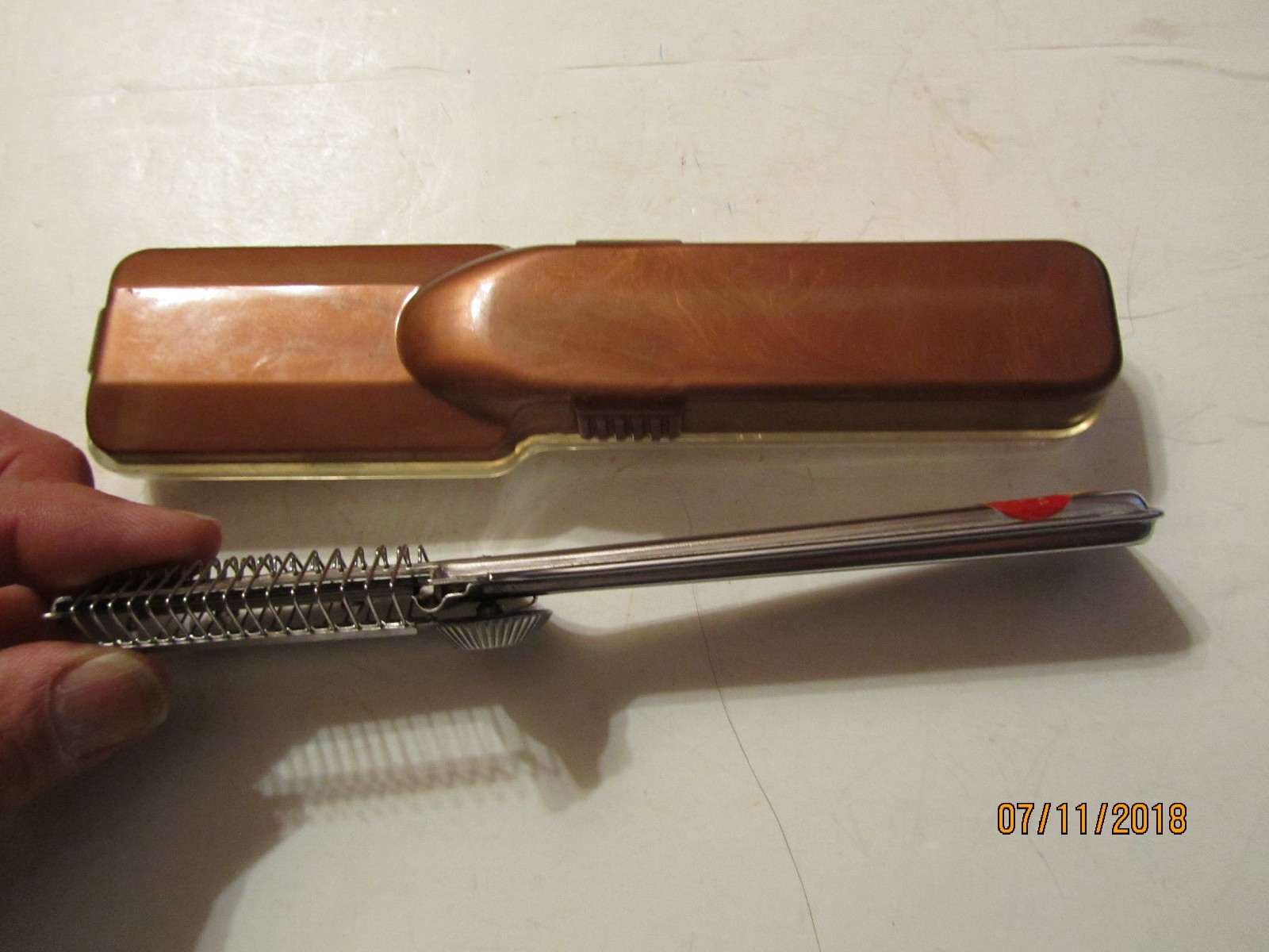 Brown vintage Playtex hair cutter with black handle in clear case, resting on white surface, text “07/11/2018” at bottom.