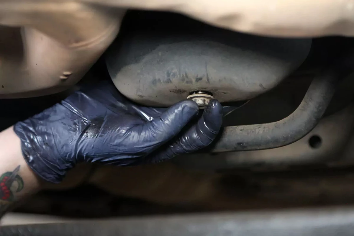 A mechanic grabbing an oil drain plug by hand.