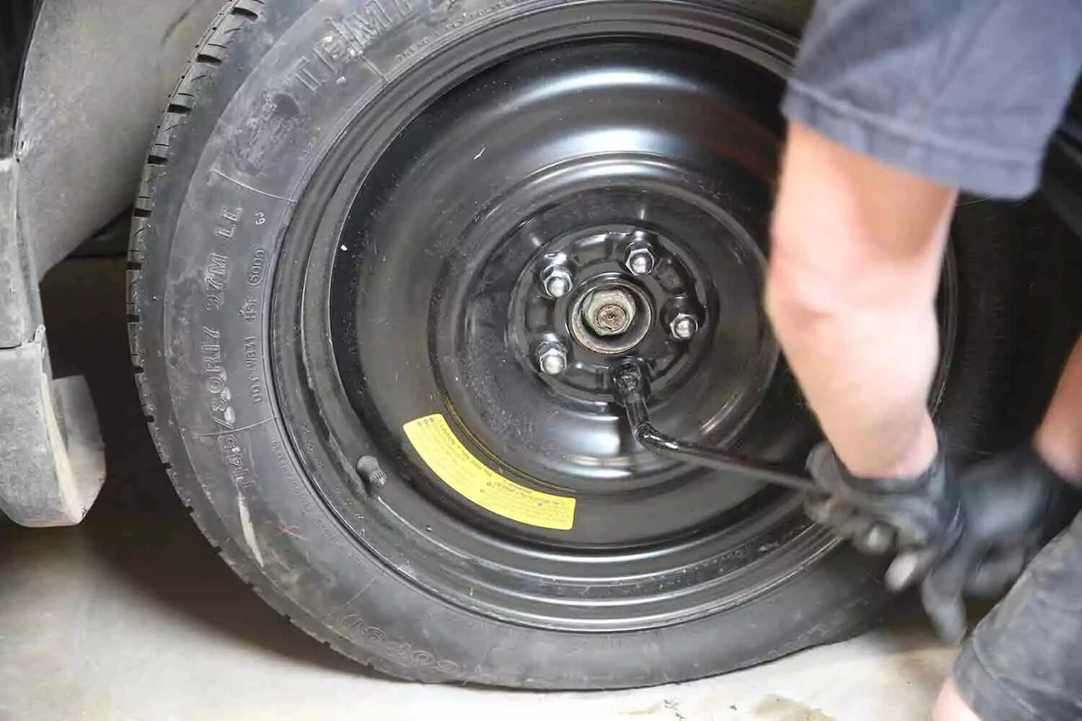 A mechanic uses a tire iron to tighten the lug nuts on a vehicle's emergency spare tire.