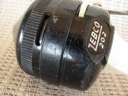 Black vintage Zebco 202 spin casting reel with worn silver handle, brass bearing, and white Zebco 202 label.