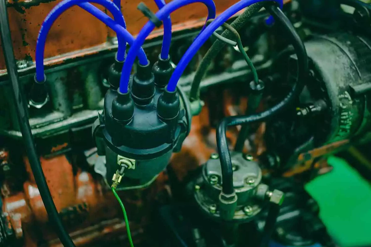 A vintage four-cylinder engine with a new distributor and vibrant blue spark plug wires.