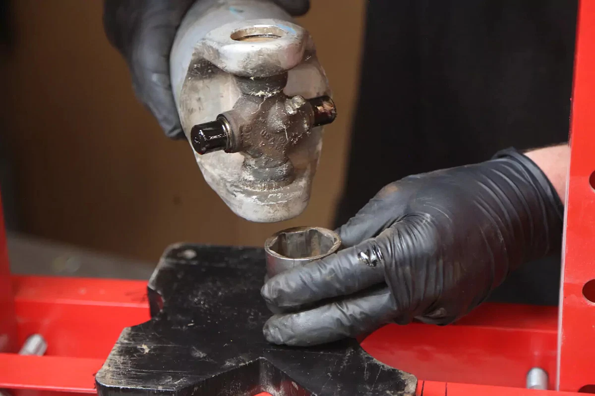 A mechanic wearing black gloves flips the driveshaft in the press.