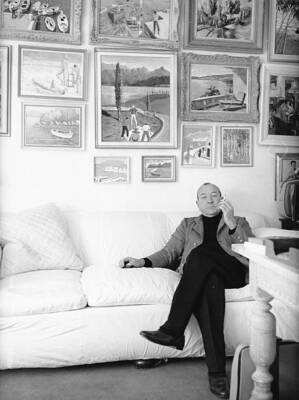 playwright Sir Noel Coward, smoking a cigarette while sitting o - 1950 Old Photo