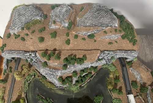 Z scale model layout with rocky cliffs, river, trees, and train tracks passing through a natural gorge.