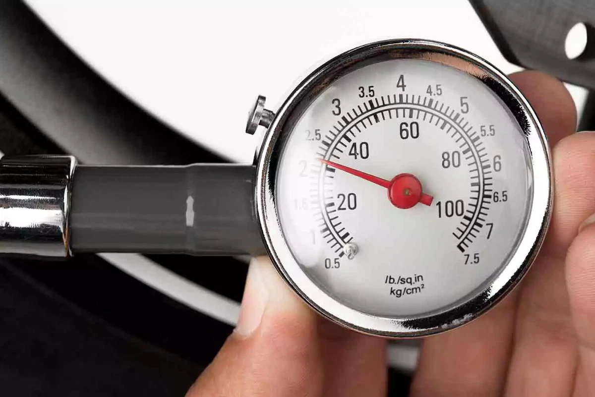 A close-up view of a driver checking tire pressure using an analog gauge with a bleeder valve.