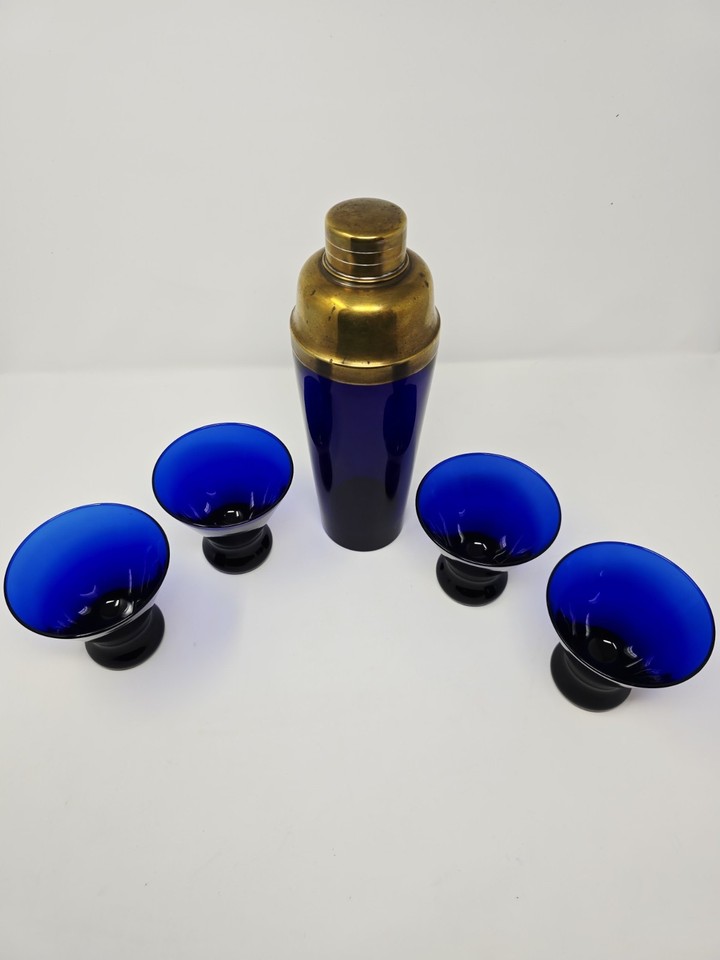 A rare matched set — deep cobalt blue glass shaker with brass hardware and matching glasses is pure Art Deco trophy-shelf material.