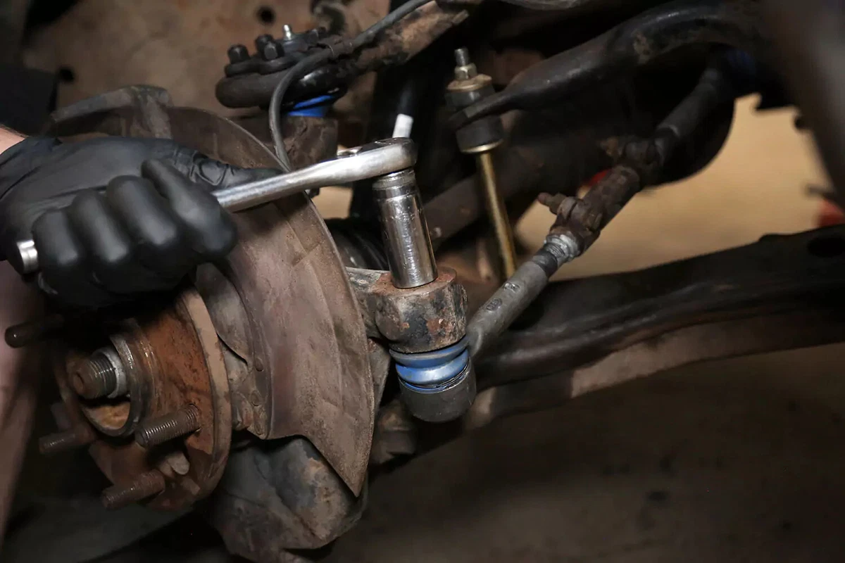 A mechanic tightens the nut on a tie rod end’s tapered pin with a socket wrench.