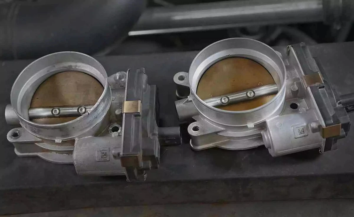 Two throttle bodies sitting on a workbench. The unit on the left is old, and the unit on the right is new.
