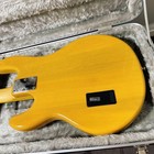 Yellow Sterling by MUSICMAN Ray 24 CA electric bass guitar with silver hardware and black pickguard, encased in gray hard shell.