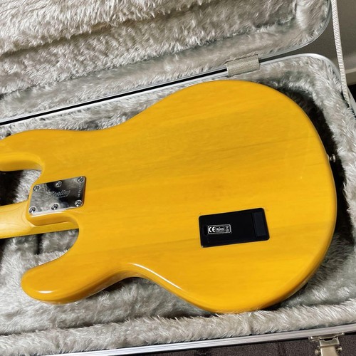 Yellow Sterling by MUSICMAN Ray 24 CA electric bass guitar with silver hardware and black pickguard, encased in gray hard shell.