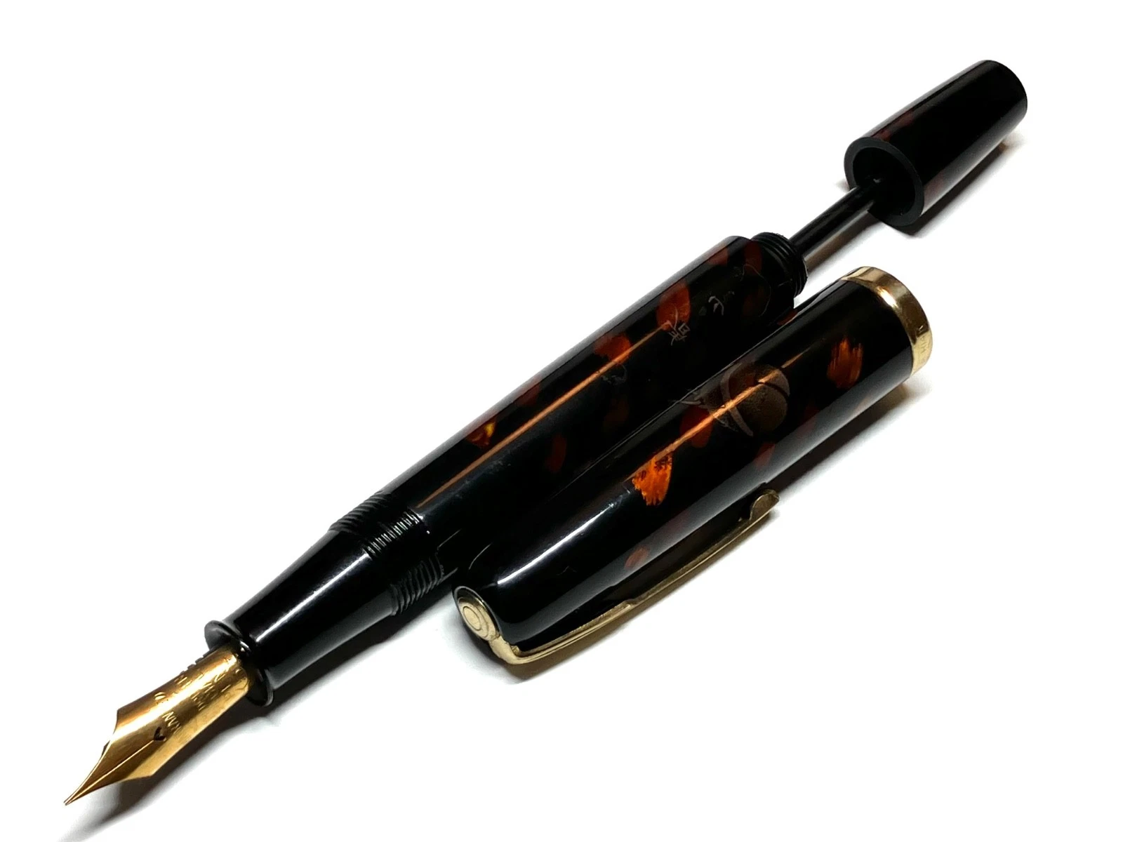 Black HARUYAMA made ink shut off fountain pen with gold accents, urushi maki-e body, and fine gold nib on white paper.