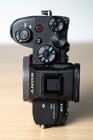 Black Sony Alpha a7S III body with top controls, dials, and gold logo, showing two black batteries on a wooden surface.