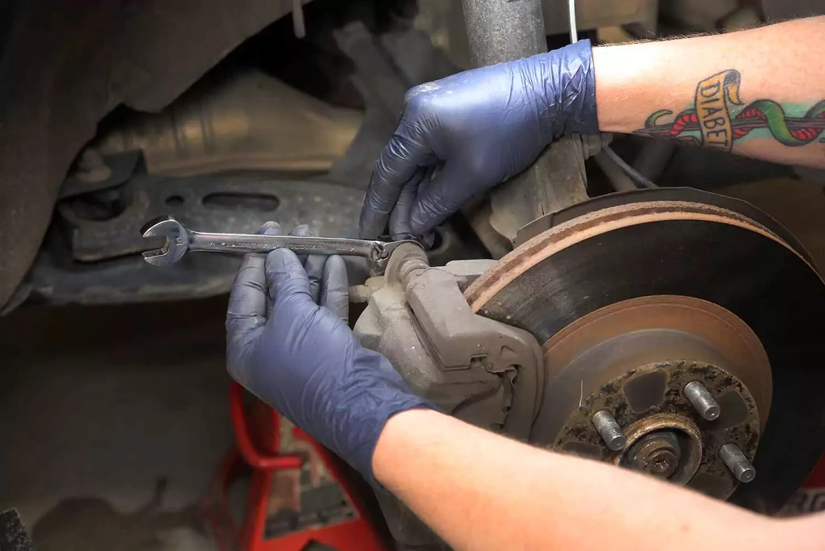 A mechanic uses a wrench on a brake caliper bolt.