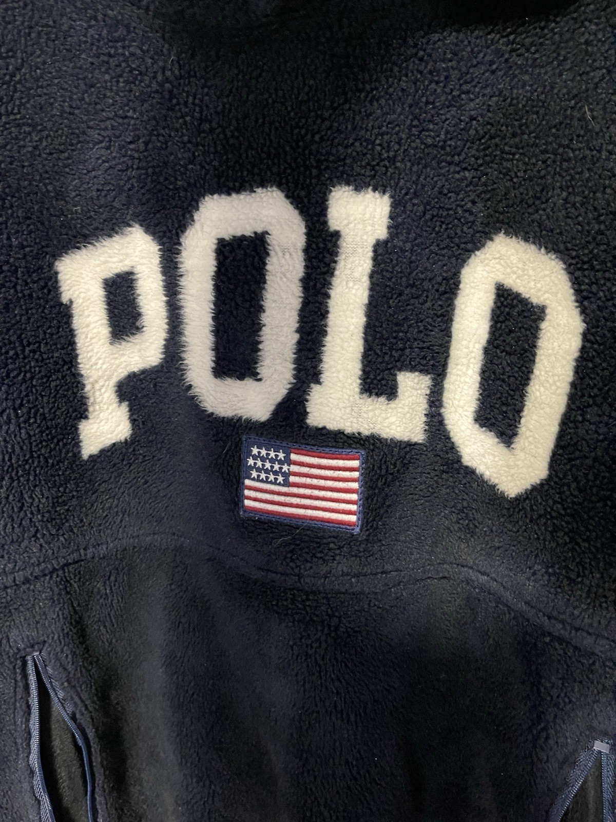 Navy fleece hoodie with cream text “POLO” and red, white, and blue American flag patch on chest.