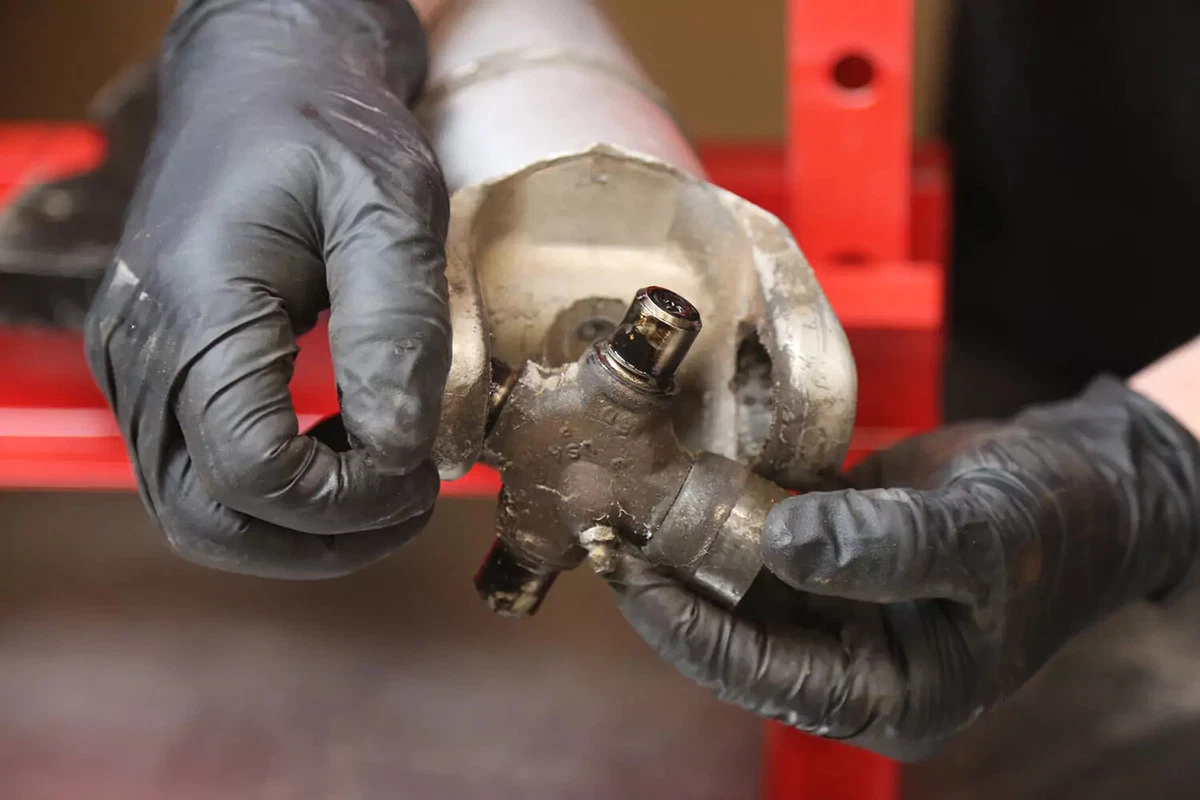 A mechanic wearing black gloves removes the joint cross.