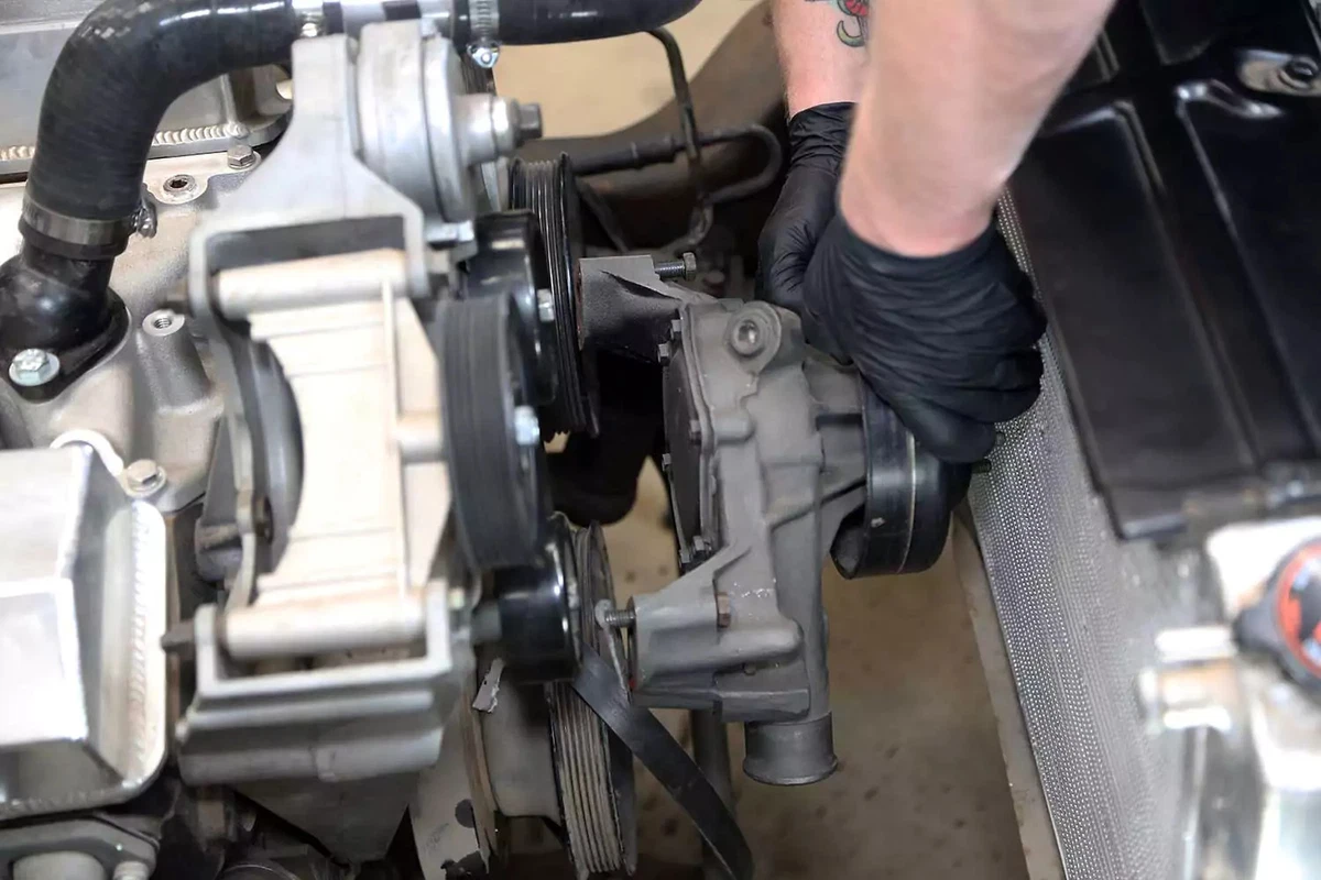 A mechanic pulls the water pump off the engine. 