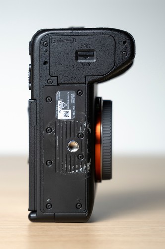 Black Sony Alpha a7S III camera back with two batteries, showing metal parts and engraved text on a wooden surface.