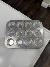 Silver 12-cup muffin pan with circular muffin cups, made in U.S.A., on a white surface with dark wood floor.