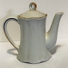 Tall white porcelain teapot with gold rim and handle, made in USA, on plain background.