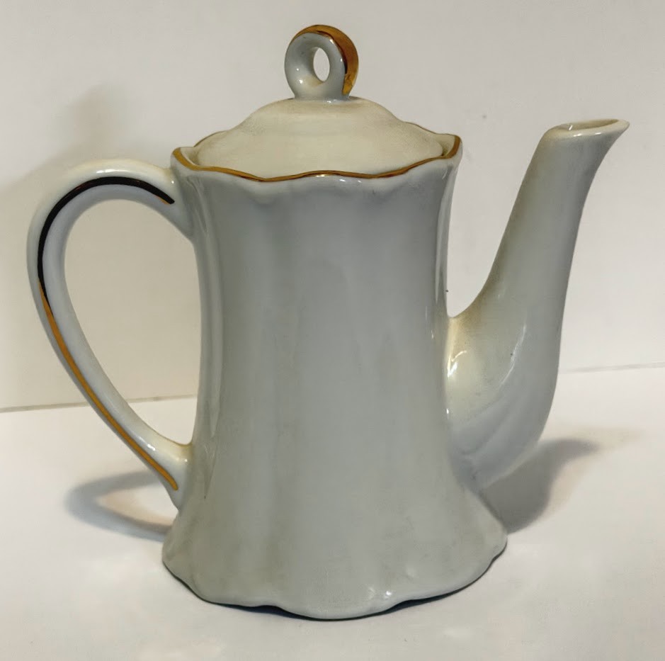 Tall white porcelain teapot with gold rim and handle, made in USA, on plain background.