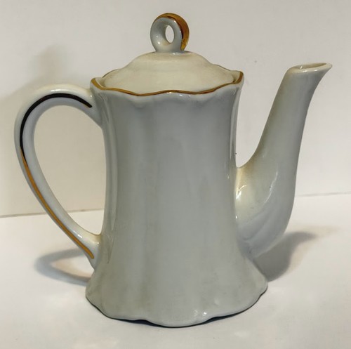 Tall white porcelain teapot with gold rim and handle, made in USA, on plain background.