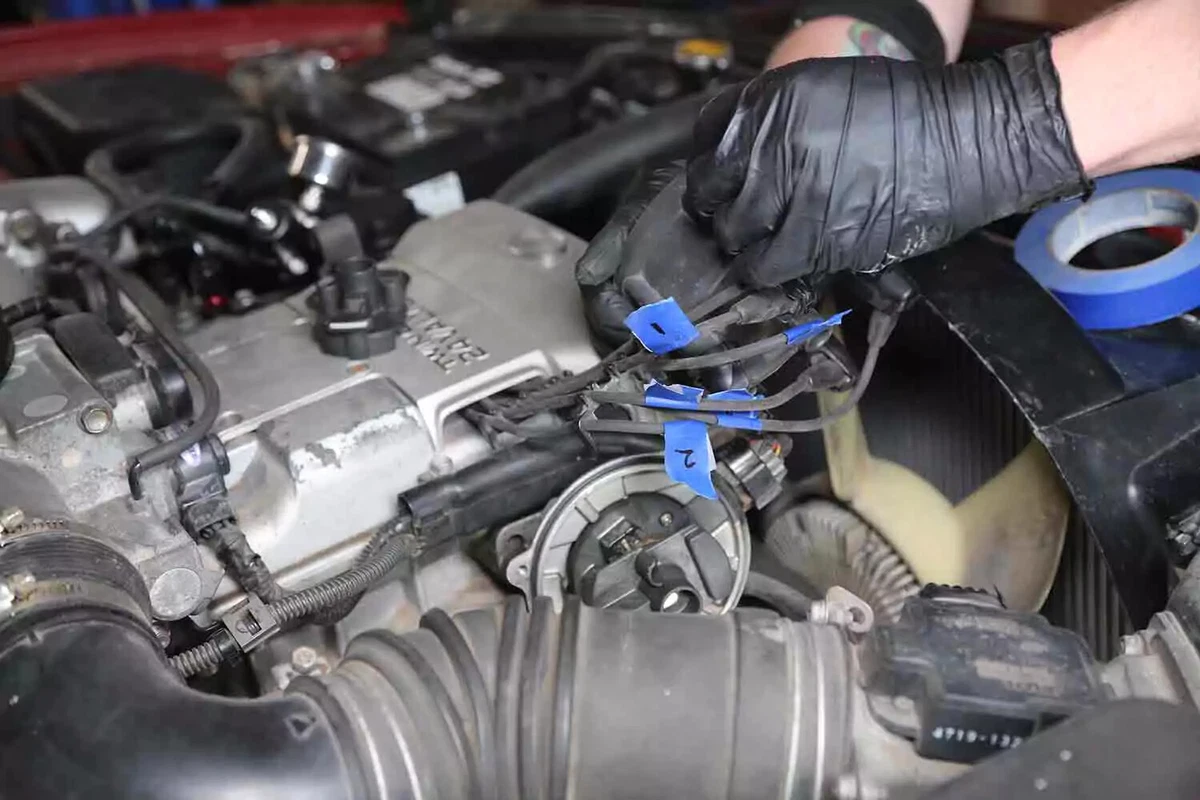 A mechanic wearing black gloves removes a vehicle's distributor cap.