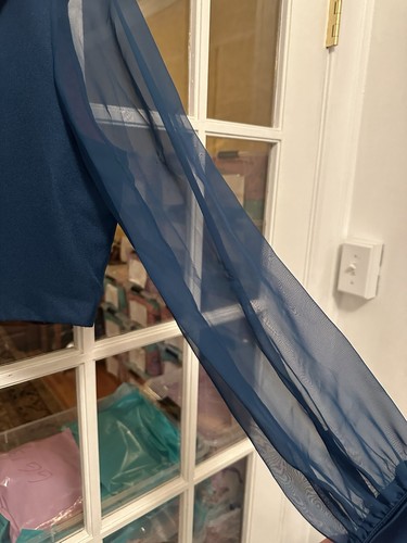 Navy blue long sleeve garment with flowing sheer fabric, displayed on a mannequin in front of a white door.