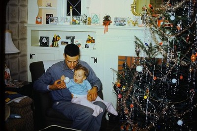 RED BORDER SLIDE Man holding baby near a retro Christmas tree.