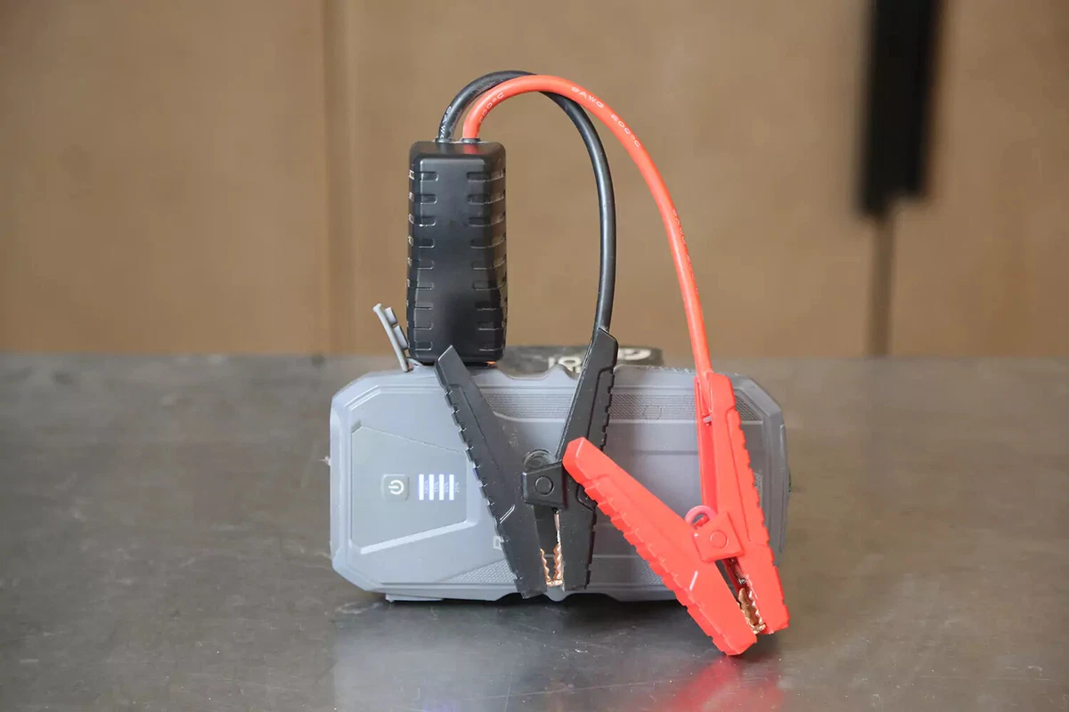 A small jump box with black and red jumper cables sits on a work surface.
