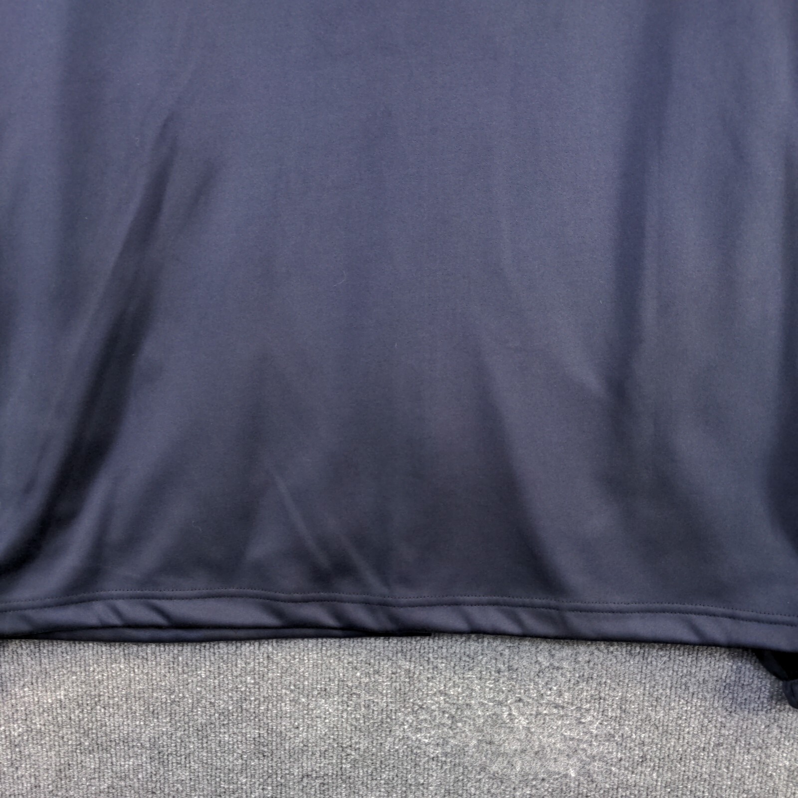 Close-up of dark blue fabric, 2XL size, with smooth surface and subtle textured hem, laid flat on gray carpet.