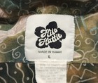 White fabric tag with black “Hilo Hattie” text, “Made in Hawaii” logo, and large letter L on green patterned background.